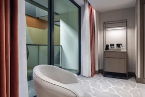 Une chambre d’hôtel dotée d’une paroi en verre, d’un coin salon, d’une petite kitchenette et d’un miroir.