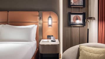 A hotel room with a bed, a bedside table with a phone and a lamp, and a wall-mounted picture frame.