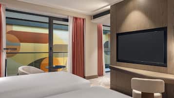 Ein Hotelzimmer mit einem großen Bett, einem an der Wand montierten Fernseher, einem kleinen Tisch und einem Sessel.