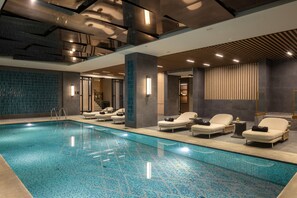 A modern indoor swimming pool with lounge chairs and a tiled floor. - Hilton Istanbul Airport (Arnavutköy)