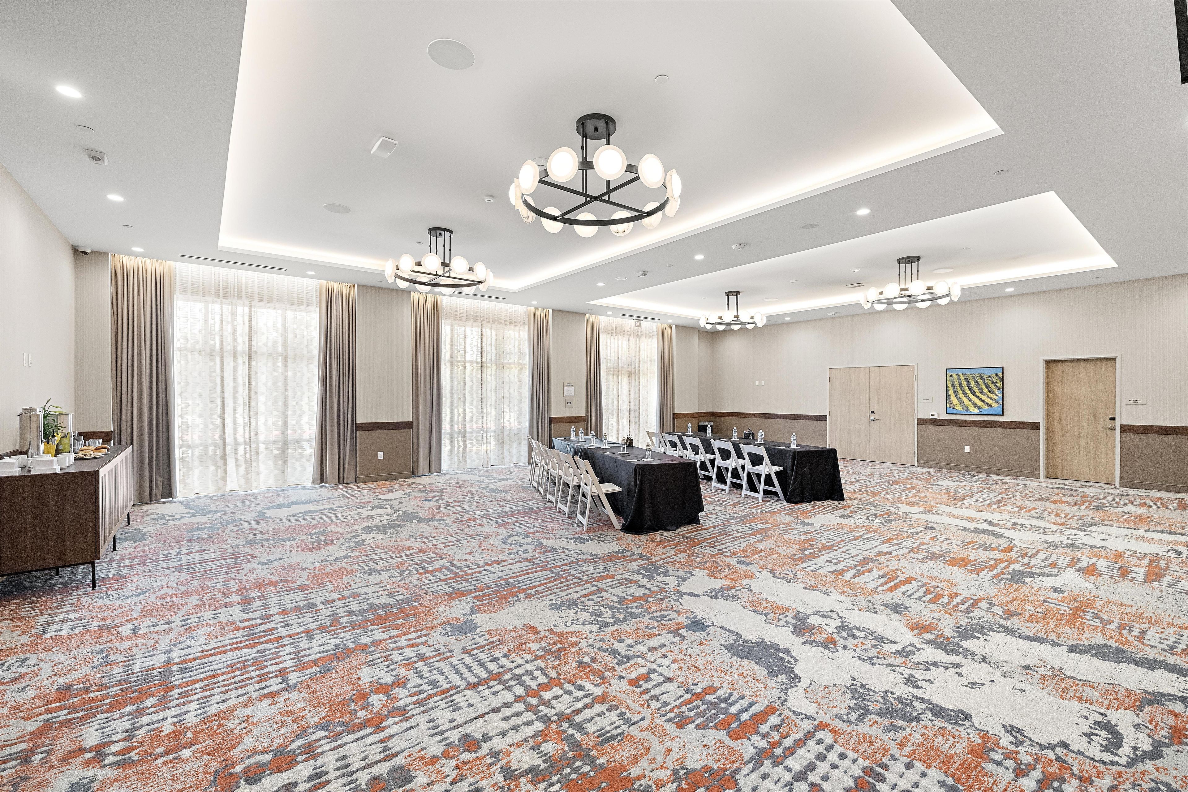 Une salle de conférence avec un tapis à motifs, une longue table entourée de chaises et un lustre.