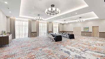 Une salle de conférence avec un tapis à motifs, une longue table entourée de chaises et un lustre.