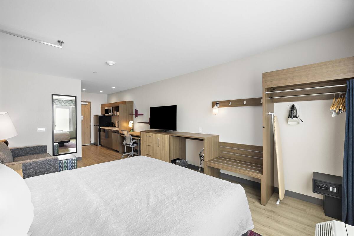 A hotel room with a bed, a desk with a computer, a TV, a mirror, a wardrobe, and a bathroom.