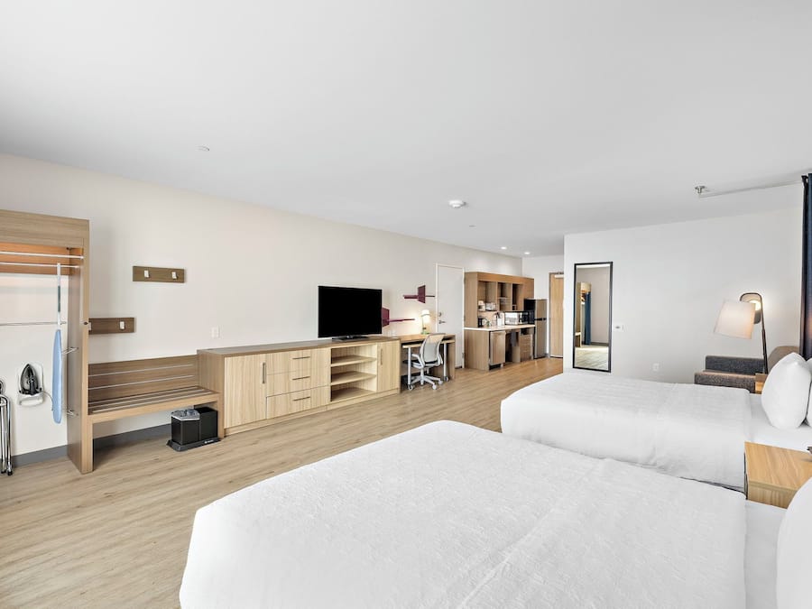 Habitación de hotel con dos camas, un escritorio, televisión, espejo y kitchenette.