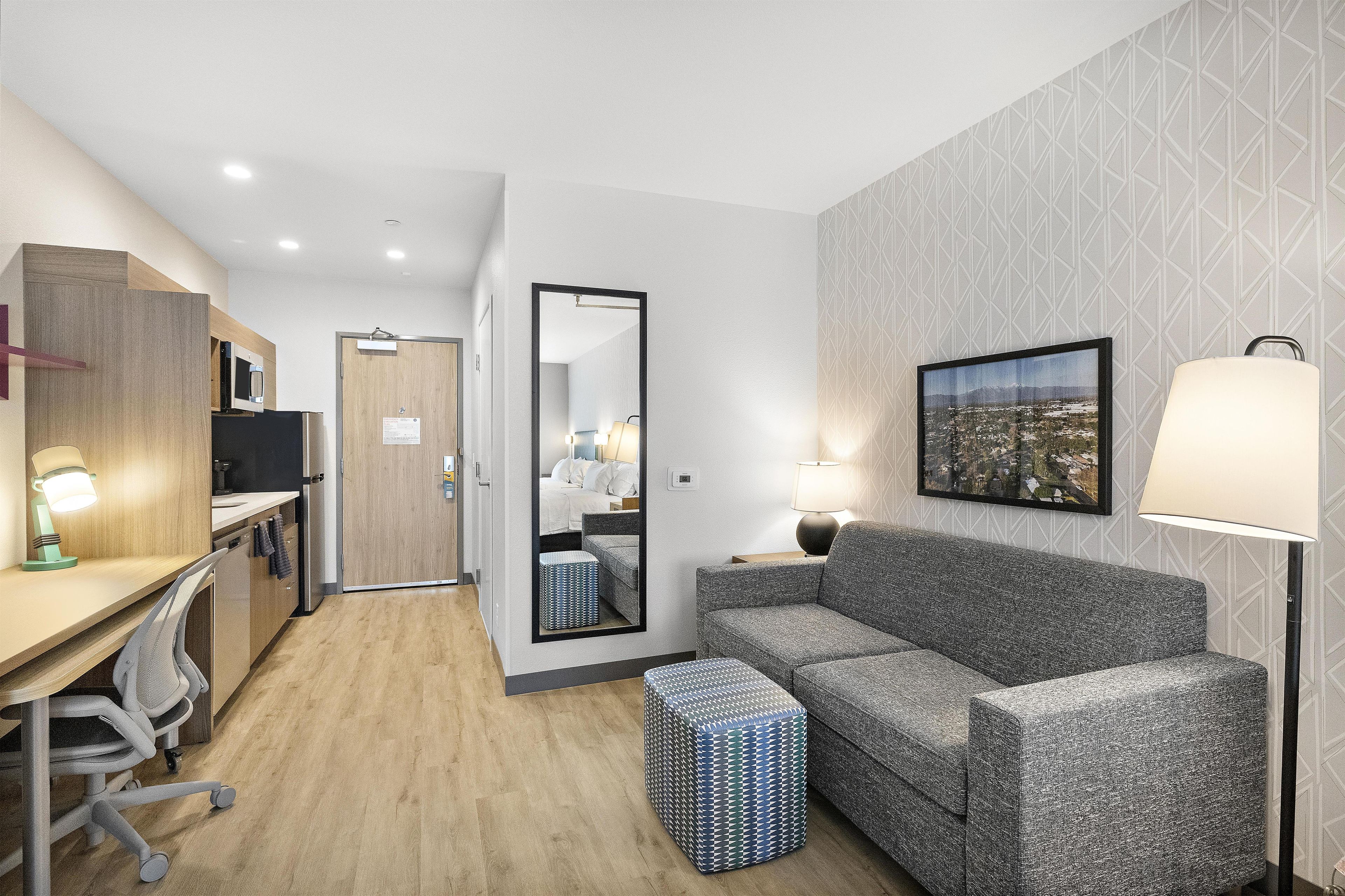 Una moderna camera d'albergo con angolo cottura, un divano, un tavolino, una lampada e un quadro appeso al muro.