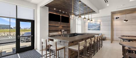 Una cocina moderna con una isla grande, taburetes de bar, iluminación colgante y vistas a través de un ventanal.