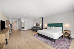 A hotel room with a bed, bedside tables, a desk, a TV, a sofa, and a patterned wall.