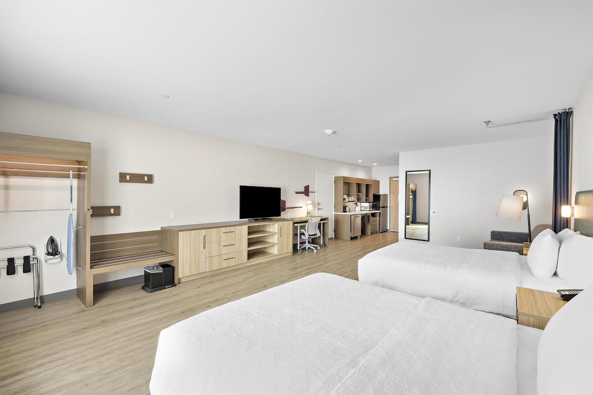 A hotel room with two beds, a desk, a television, and a kitchenette.