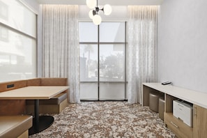 A compact room with a dining table, a bench, a kitchenette, and a large window with curtains. - Home2 Suites by Hilton Ontario Airport (Ontario)