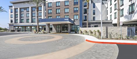 Un hotel moderno con un camino de entrada curvo, varios pisos y un asta de banderas.