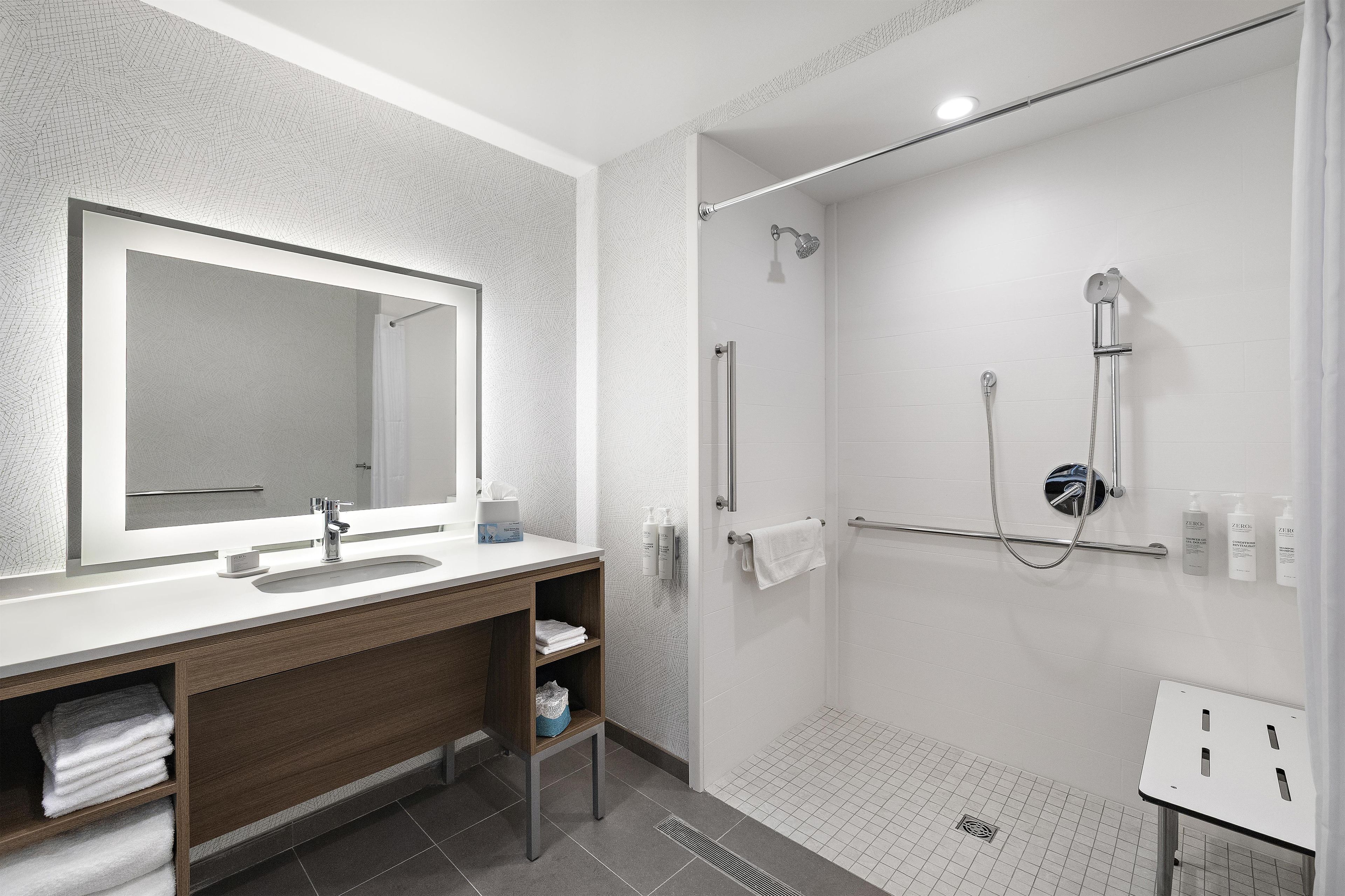 Un baño moderno con un espejo grande, un lavamanos, una ducha con cabezal de ducha manual y un perchero para toallas.
