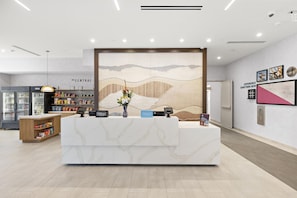 A hotel reception area with a marble counter, a floral centerpiece, and a wall-mounted artwork depicting a mountainous landscape. - Home2 Suites by Hilton Ontario Airport (Ontario)