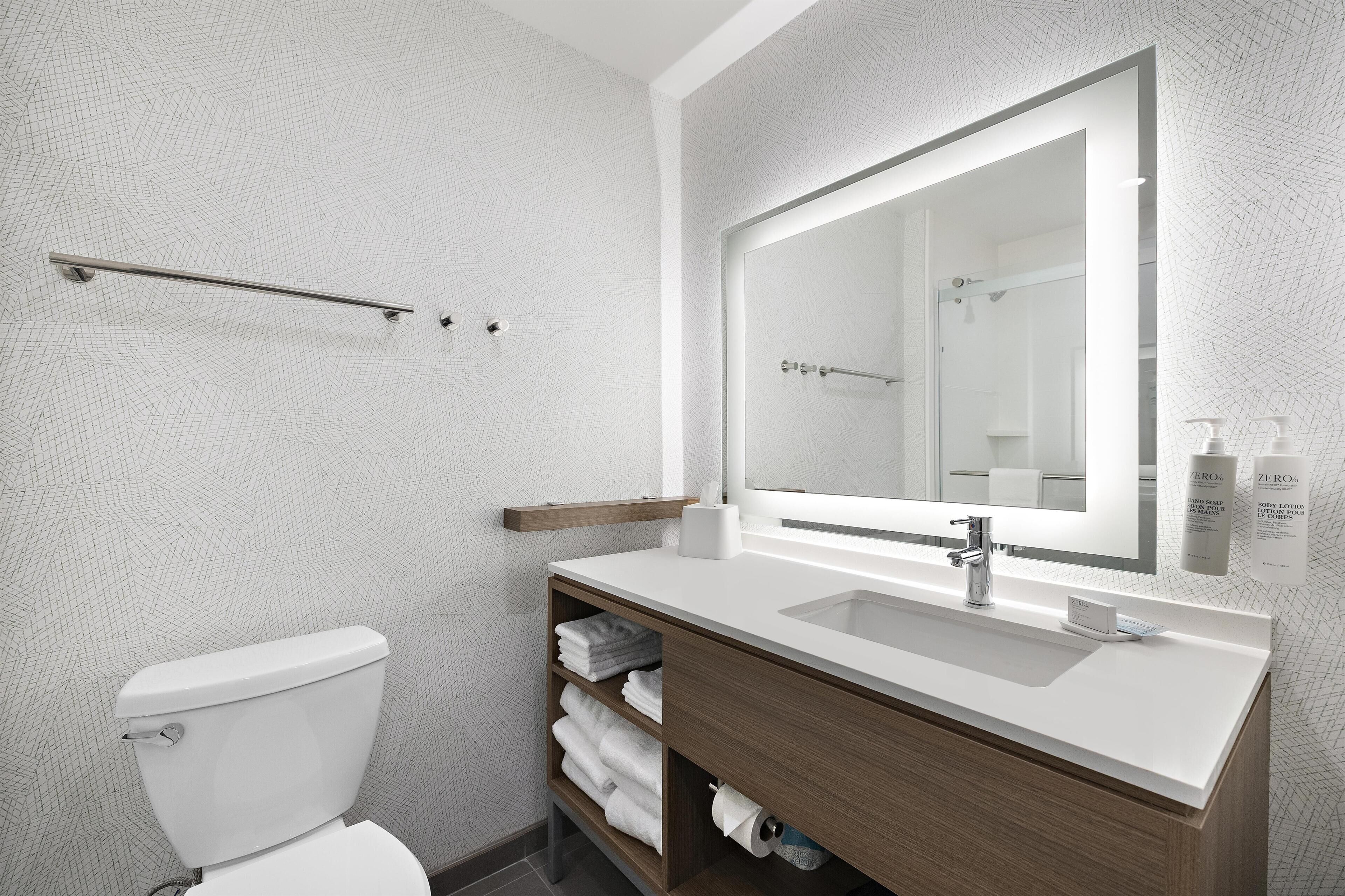 Un baño moderno con inodoro, lavamanos, espejo y toallero.