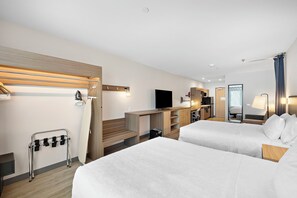 A hotel room with two beds, a TV, a desk, and a mirror.