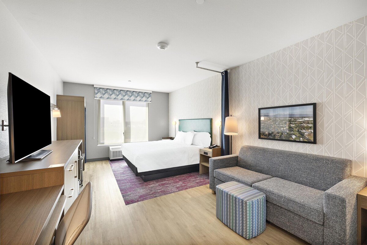 A hotel room with a bed, a sofa, a TV, a desk, and a window.