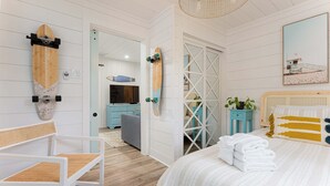 Un dormitorio con cama, una silla, un monopatín colgado en la pared, un televisor y una puerta que da a otra habitación.