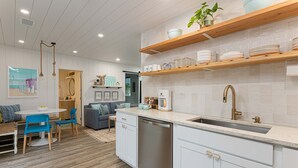 Una cocina moderna con armarios blancos, lavavajillas y estantes de madera con vajilla y vasos.