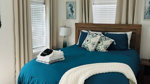 A bedroom with a wooden bed, teal bedding, a white throw blanket, and a nightstand with a lamp.