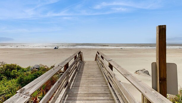 Una passerella in legno che conduce a una spiaggia, con cielo sereno.