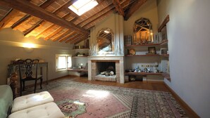 Um quarto amplo no sótão com vigas de madeira aparentes, lareira e um tapete grande.
