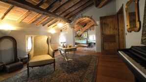 Um quarto amplo com teto alto, vigas de madeira aparentes, um piano de cauda, uma poltrona confortável e um tapete tradicional.