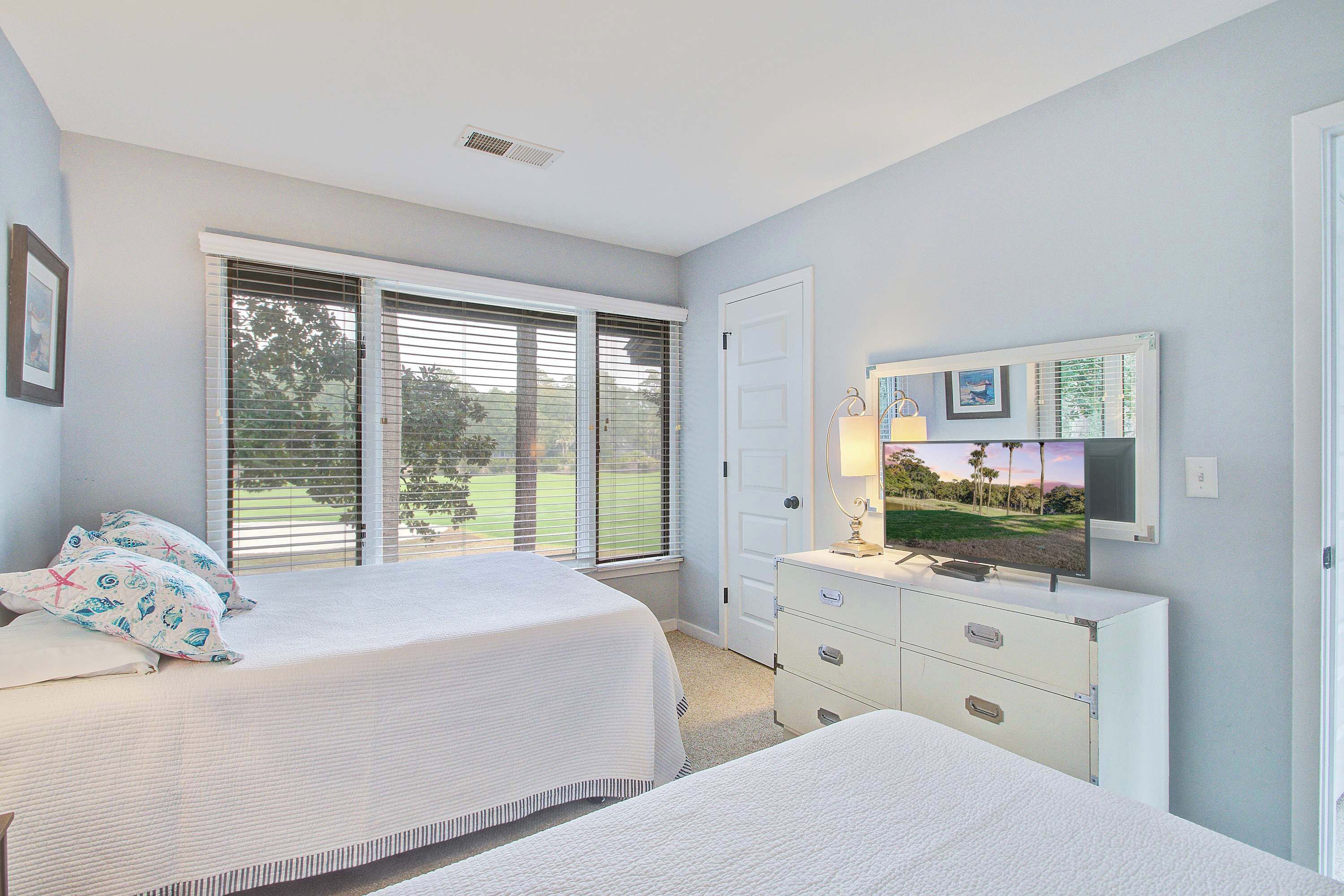 A bedroom with a bed, a dresser, a television, and a door leading to a balcony.