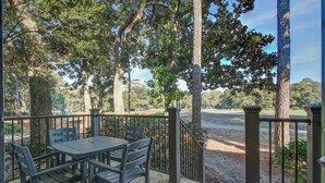 A wooden deck with a table and chairs, surrounded by trees and a view of a golf course.
