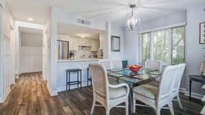 A modern kitchen with white cabinetry, a glass dining table, and wicker chairs.