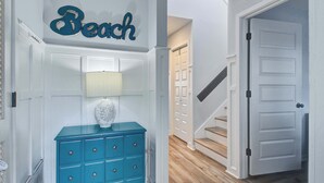 A hallway with a blue dresser, a wall-mounted lamp, and a door labeled 'Beach.'