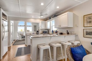 A modern kitchen with white cabinetry, a central island with stools, a microwave, and a coffee maker.