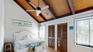 A bedroom with a bed, a ceiling fan, a painting, a window, and a wooden floor. - Comfy Golf View Cottage with WiFi, a Shared Pool, Central AC, Private Washer/Dryer (Seabrook Island)