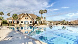 A large swimming pool with clear blue water, surrounded by palm trees and a building with a tiled roof. - Comfy Golf View Cottage with WiFi, a Shared Pool, Central AC, Private Washer/Dryer (Seabrook Island)