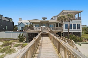 A wooden boardwalk leading to a beachfront property with multiple levels, a balcony, and a palm tree. - Luxury, Dog-Friendly, Oceanfront Home on Folly Beach (Folly Beach)