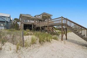 A beachfront property with a wooden deck, multiple levels, and a sandy beach area.
