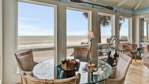 A spacious room with large windows overlooking a beach, furnished with wicker chairs and a glass table. - Luxury, Dog-Friendly, Oceanfront Home on Folly Beach (Folly Beach)