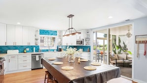 Una cocina moderna con armarios blancos, una mesa de comedor de madera y un salpicadero azul.