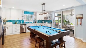 Una cocina moderna con mesa de billar, armarios blancos y un ventanal grande.