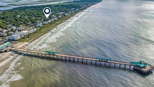 Vista aérea de una zona costera con un muelle largo que se extiende sobre el agua, rodeado de edificios residenciales y vegetación.