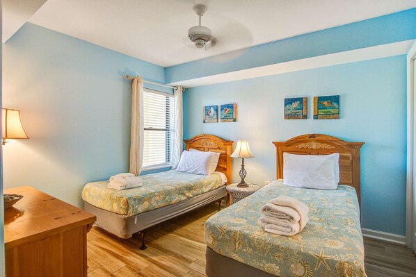 A room with two beds, a wooden desk, a ceiling fan, and a window with blinds. - Oceanfront, first-floor villa w/large balcony & shared pool - near the beach (Folly Beach)