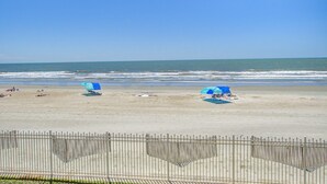 Une plage avec une clôture, quelques parasols et l’océan en arrière-plan.