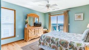 Une chambre à coucher comprenant un lit, une commode, un ventilateur de plafond, une fenêtre avec des stores et une vue sur l’océan.