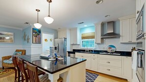 Una cocina moderna con armarios blancos, una isla central y un comedor con sillas de mimbre.