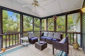 A sunroom with a large window, wicker furniture, and a ceiling fan. - Peaceful Isle of Palms escape with grill and patio (Isle of Palms)