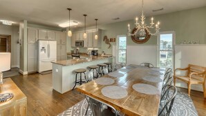 A spacious kitchen with a central island, bar stools, and a chandelier. - Raised oceanfront home with elevator & outdoor shower just steps from beach (Folly Beach)