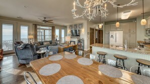 A spacious living room with a wooden dining table, a chandelier, and a view of the ocean. - Raised oceanfront home with elevator & outdoor shower just steps from beach (Folly Beach)
