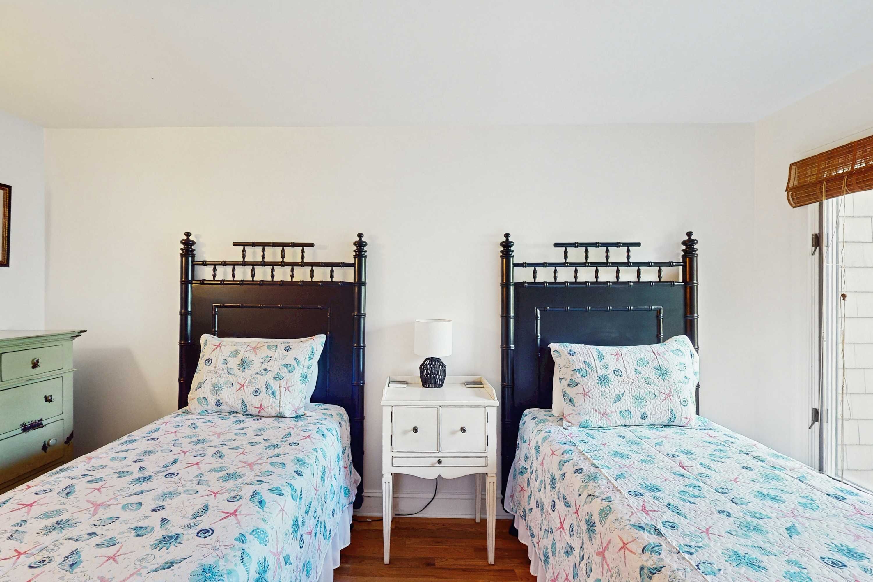A bedroom with two beds, each with a headboard, a bedside table with a lamp, and a dresser.