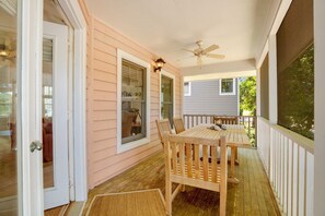 A wooden deck with a table and chairs, a ceiling fan, and a door leading inside. - Casual cottage w/screened porch & shared pool - walk to the beach (Isle of Palms)