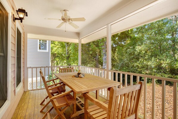 A covered porch with a wooden table and chairs, a ceiling fan, and a view of trees. - Casual cottage w/screened porch & shared pool - walk to the beach (Isle of Palms)