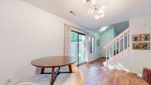 Ein Essbereich mit einem runden Tisch und gepolsterten Bänken, eine Treppe mit weißen Geländern und ein Blick ins Freie durch große Fenster.
