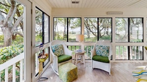 Un solárium con ventanas amplias, muebles de mimbre y una pequeña mesa con lámpara.